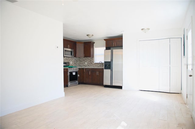 kitchen featuring light countertops, decorative backsplash, appliances with stainless steel finishes, a sink, and dark brown cabinetry