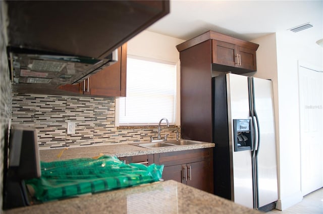 kitchen featuring stainless steel refrigerator with ice dispenser, visible vents, backsplash, a sink, and dark brown cabinetry