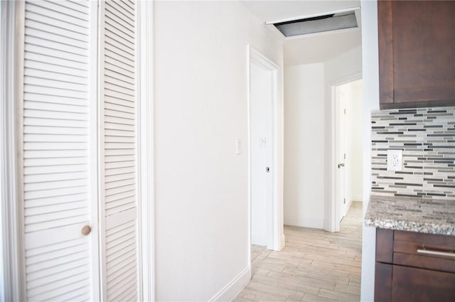 hall featuring light wood-type flooring, attic access, and baseboards