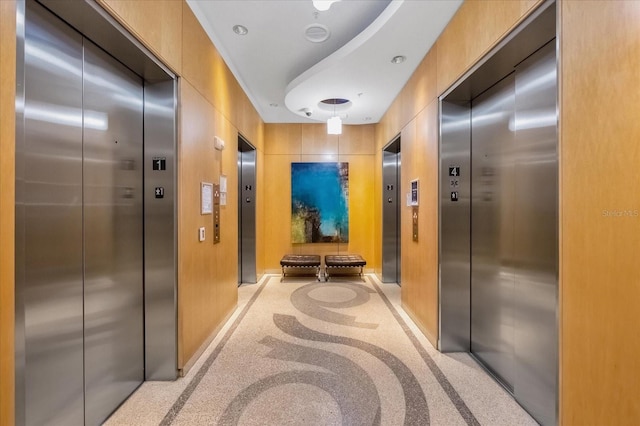 hall with baseboards, elevator, and light speckled floor