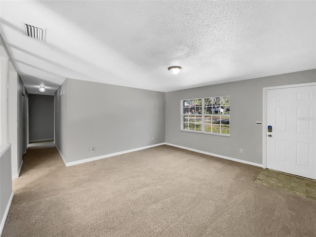 unfurnished room with a textured ceiling, carpet floors, visible vents, and baseboards