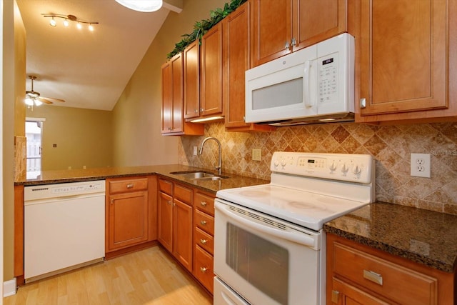 kitchen featuring brown cabinetry, white appliances, a sink, and dark stone countertops