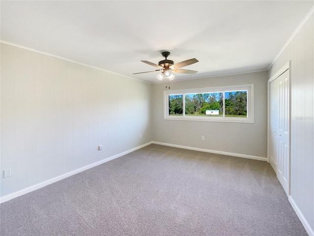 carpeted spare room with ceiling fan, baseboards, and crown molding