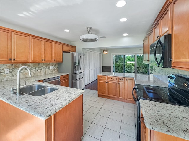 kitchen featuring light tile patterned flooring, a peninsula, a sink, black appliances, and brown cabinetry