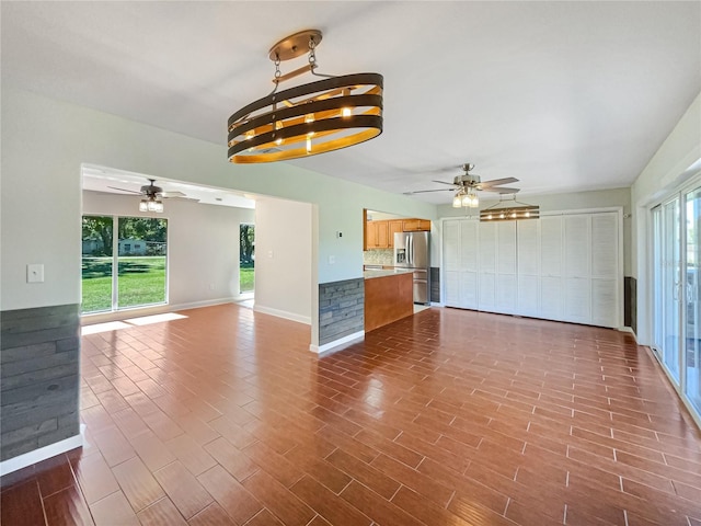 unfurnished living room with ceiling fan with notable chandelier, dark wood-type flooring, and baseboards