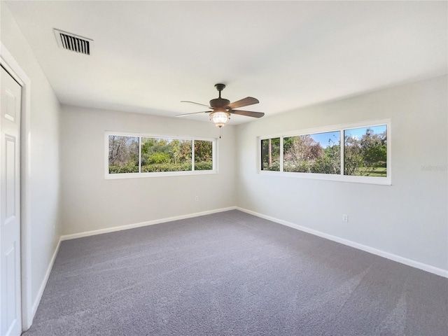 empty room featuring dark colored carpet, visible vents, ceiling fan, and baseboards