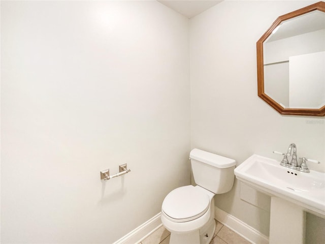 half bath featuring a sink, toilet, baseboards, and tile patterned floors