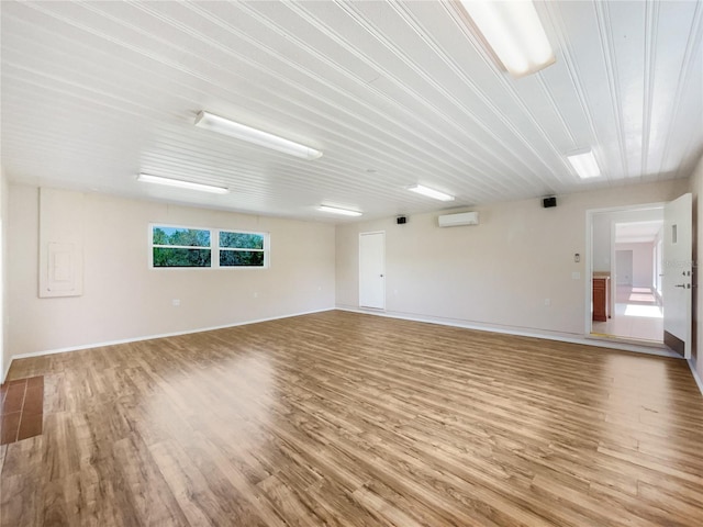 unfurnished room featuring a wall mounted AC, wood finished floors, and baseboards