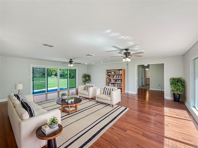 living room featuring a ceiling fan, light wood-type flooring, visible vents, and baseboards