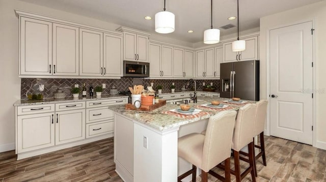 kitchen with tasteful backsplash, visible vents, wood finished floors, stainless steel appliances, and a sink