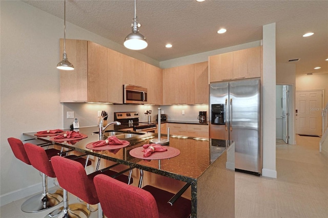 kitchen featuring a sink, a peninsula, appliances with stainless steel finishes, and light brown cabinets