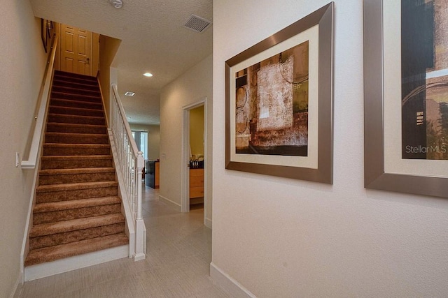 corridor with baseboards, visible vents, stairway, a textured ceiling, and recessed lighting