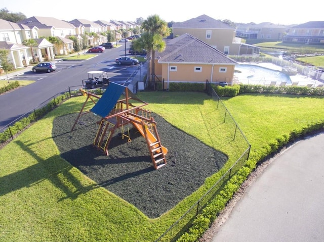 view of playground featuring a lawn, fence, and a residential view