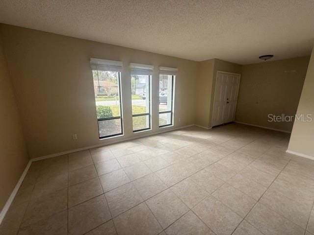 spare room with a textured ceiling, light tile patterned floors, and baseboards