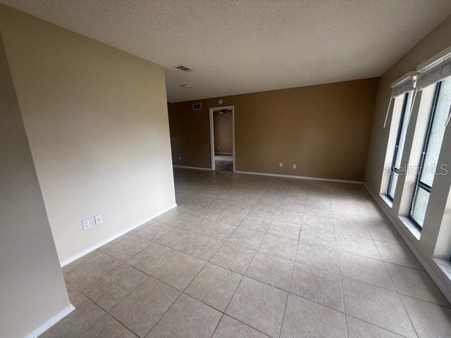 unfurnished room with visible vents, a textured ceiling, baseboards, and light tile patterned floors