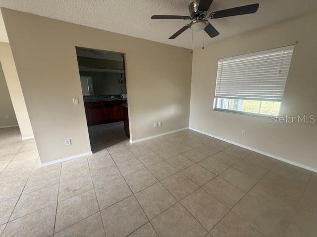 tiled empty room with a ceiling fan, a textured ceiling, and baseboards