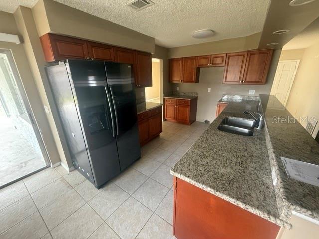 kitchen featuring light stone counters, light tile patterned flooring, a sink, black fridge with ice dispenser, and visible vents