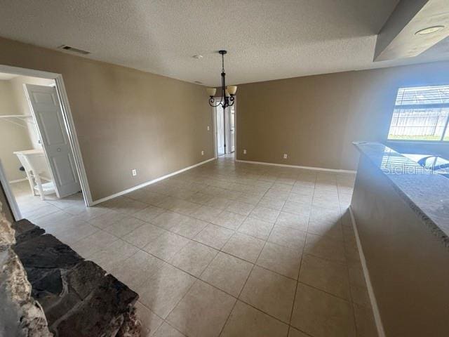 unfurnished dining area featuring visible vents, a notable chandelier, a textured ceiling, and baseboards