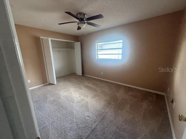 unfurnished bedroom with a textured ceiling, ceiling fan, baseboards, a closet, and carpet