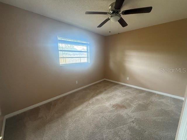 carpeted spare room with a ceiling fan, baseboards, and a textured ceiling