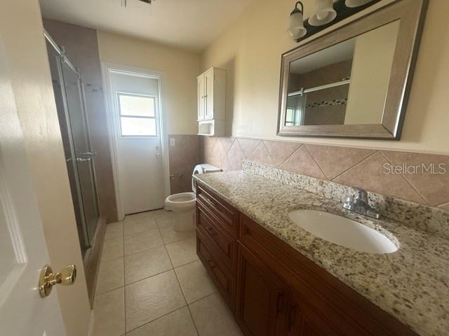 bathroom featuring toilet, tile walls, vanity, tile patterned floors, and a stall shower