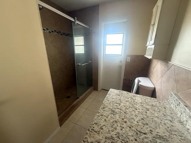 bathroom with toilet, tile patterned flooring, a shower stall, and tile walls