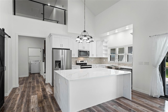 kitchen with a center island, open shelves, a barn door, appliances with stainless steel finishes, and washer / dryer