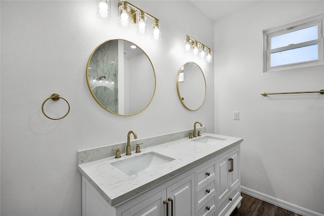 full bath featuring double vanity, baseboards, a sink, and wood finished floors