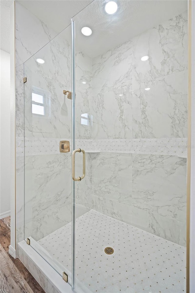 full bathroom with a marble finish shower and wood finished floors