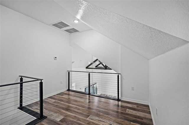 additional living space with lofted ceiling, visible vents, a textured ceiling, wood finished floors, and baseboards