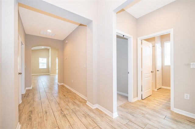 corridor with light wood-type flooring, visible vents, arched walkways, and baseboards