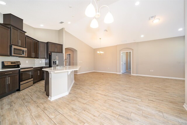 kitchen with light wood finished floors, appliances with stainless steel finishes, arched walkways, and a notable chandelier