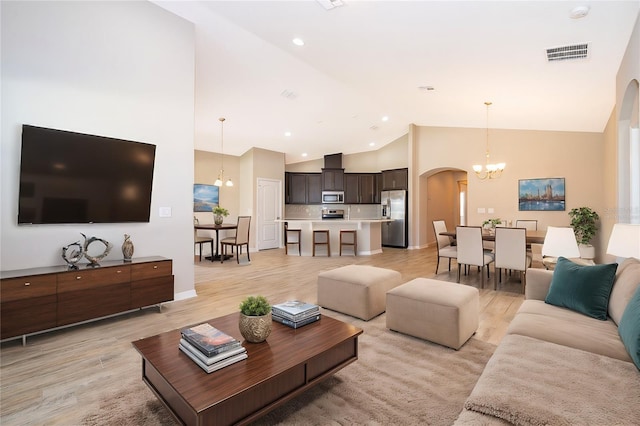 living area with visible vents, arched walkways, an inviting chandelier, light wood-type flooring, and high vaulted ceiling