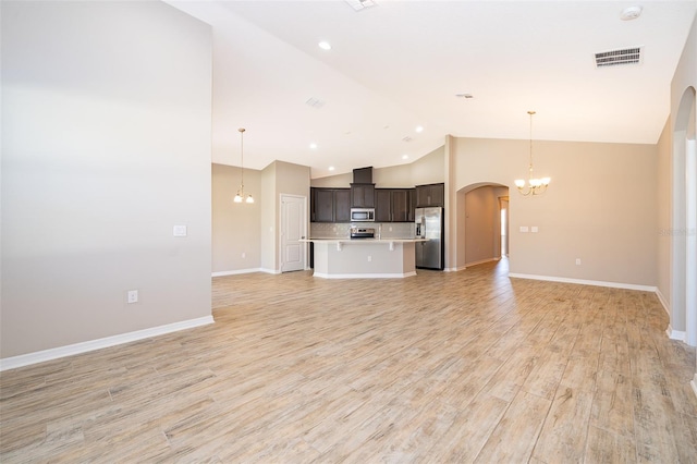 unfurnished living room with a chandelier, arched walkways, visible vents, baseboards, and light wood-style floors