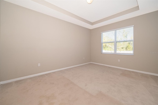 empty room featuring baseboards, a tray ceiling, and light colored carpet