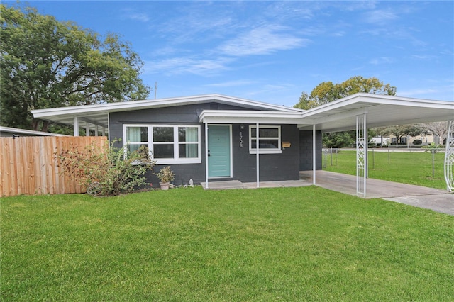 view of front of home with a carport, concrete block siding, fence, and a front lawn