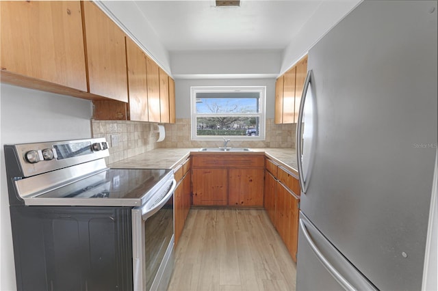 kitchen with tasteful backsplash, light wood-style flooring, appliances with stainless steel finishes, light countertops, and a sink