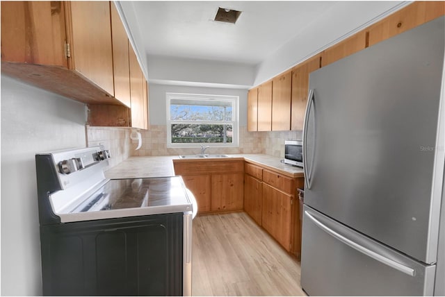 kitchen with decorative backsplash, light wood-style flooring, stainless steel appliances, light countertops, and a sink