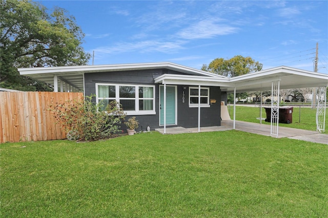 view of front facade featuring a front lawn, concrete block siding, fence, and an attached carport