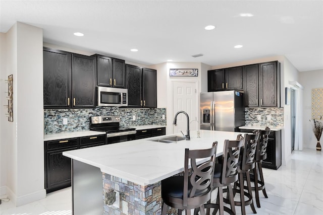 kitchen with a center island with sink, a kitchen breakfast bar, marble finish floor, stainless steel appliances, and a sink