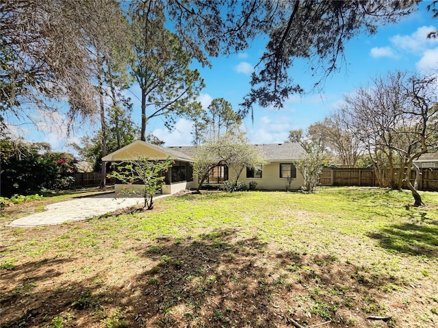 back of house with driveway, a lawn, a patio, a fenced backyard, and an attached carport