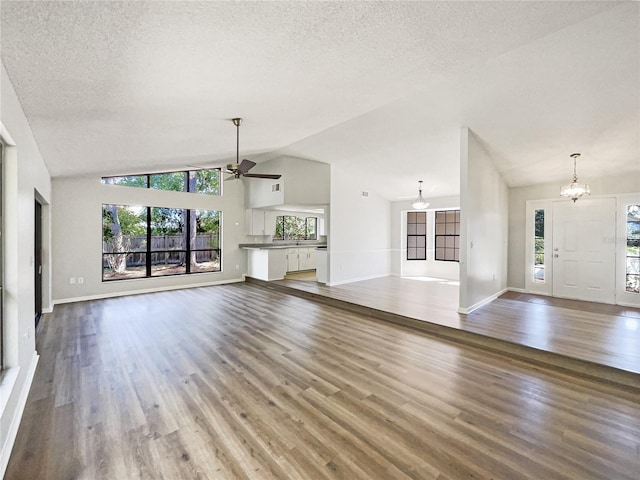 unfurnished living room featuring a wealth of natural light, a textured ceiling, wood finished floors, and ceiling fan with notable chandelier