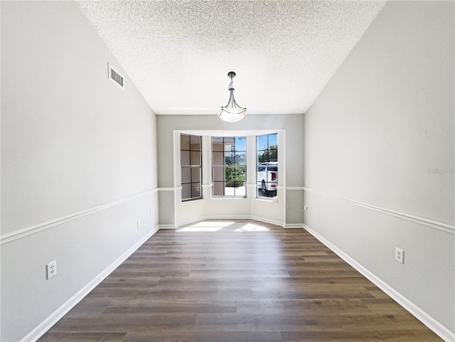 unfurnished dining area with visible vents, dark wood finished floors, a textured ceiling, and baseboards