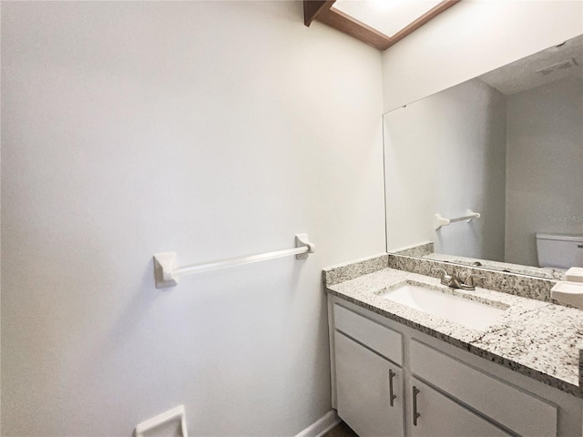 half bathroom with toilet, a skylight, vanity, and baseboards