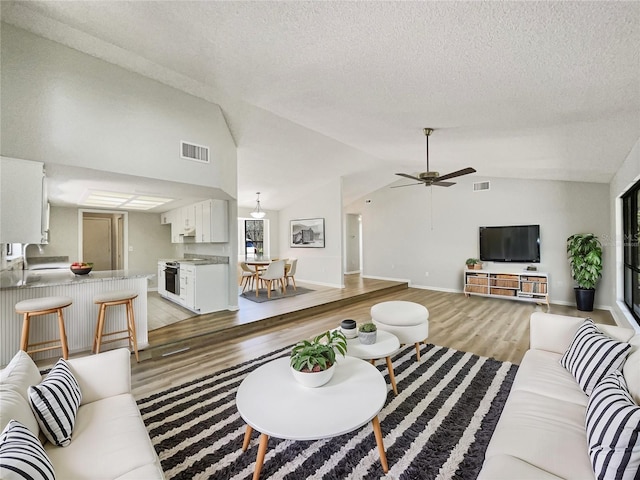 living area featuring lofted ceiling, visible vents, light wood-style flooring, and a textured ceiling