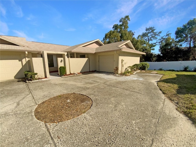 view of front of home with stucco siding, driveway, an attached garage, and fence