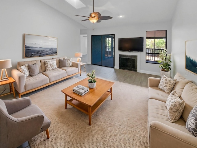 living room featuring vaulted ceiling with skylight, baseboards, ceiling fan, wood finished floors, and a fireplace