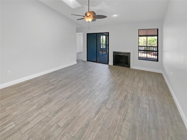 unfurnished living room featuring light wood-style floors, baseboards, a fireplace, and lofted ceiling with skylight