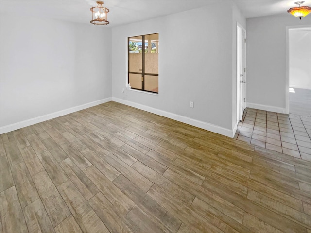 spare room featuring an inviting chandelier, wood finished floors, and baseboards