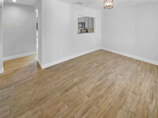 interior space with light wood-type flooring, visible vents, baseboards, and an inviting chandelier